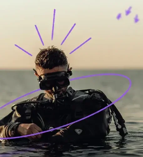 Plongeur bouteille au 3/4 dans la mer, équipé, vérifiant sa montre avant de s'immerger complètement. A la manière des sportifs de haut niveau, Prefera vous accompagne à travailler votre mental pour booster vos performances commerciales et managériales.